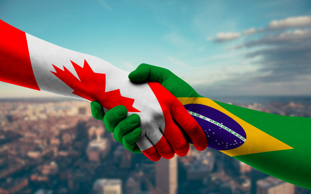Aperto de duas mãos pintadas com as cores das bandeiras do Canadá e do Brasil. O aperto simboliza a parceria entre os países.